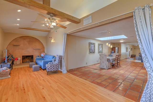 living room featuring light hardwood / wood-style flooring, ceiling fan, lofted ceiling with skylight, and a fireplace