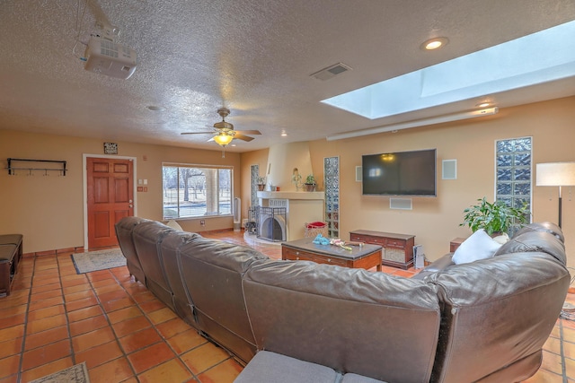 tiled living room with ceiling fan, a textured ceiling, and a skylight