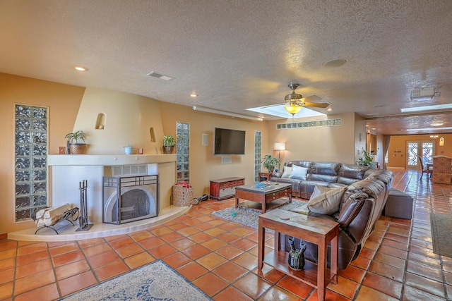 tiled living room featuring ceiling fan, a textured ceiling, and a tiled fireplace