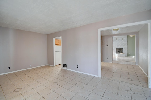 spare room with light tile patterned floors, a textured ceiling, a brick fireplace, and baseboards