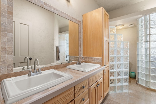 bathroom featuring double vanity, visible vents, a sink, and a textured wall