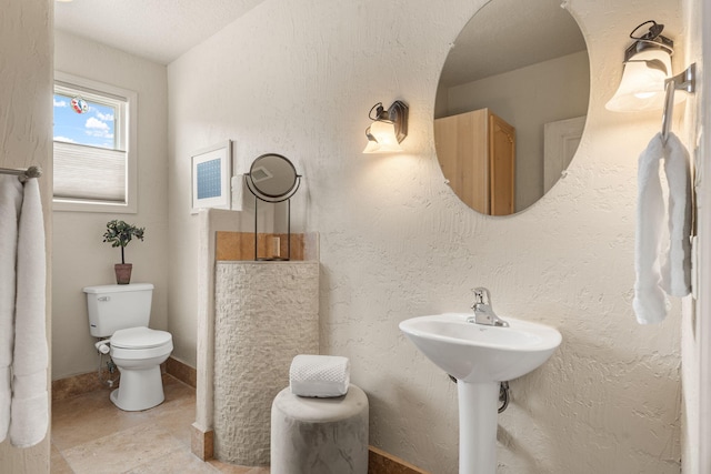 bathroom with toilet, baseboards, a textured ceiling, and a textured wall