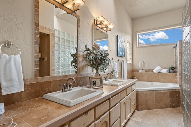 full bath with a textured wall, tiled tub, a sink, and tile patterned floors