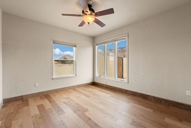 spare room with a ceiling fan, baseboards, wood finished floors, and a textured wall