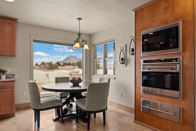 dining area featuring a chandelier, a textured wall, a textured ceiling, and baseboards