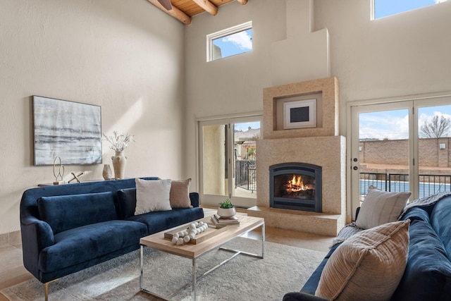 living area with a warm lit fireplace, wood ceiling, a high ceiling, and beam ceiling