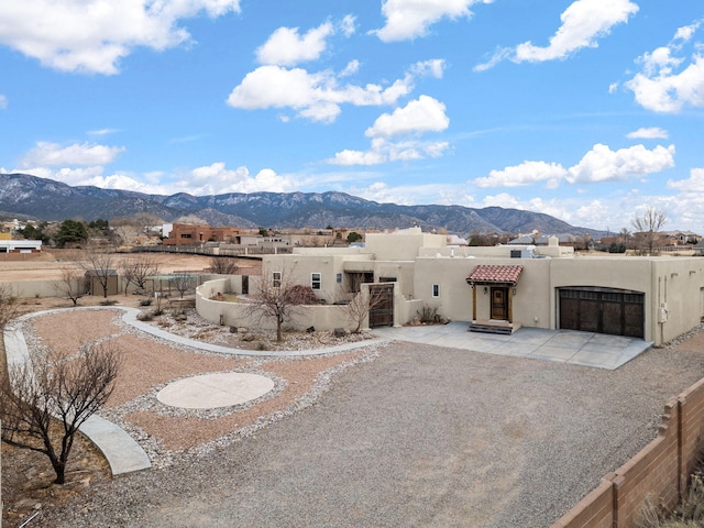 view of front of home with driveway, an attached garage, fence, a mountain view, and stucco siding