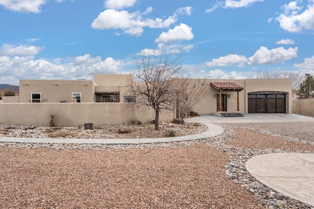 pueblo revival-style home featuring an attached garage, driveway, a fenced front yard, and stucco siding