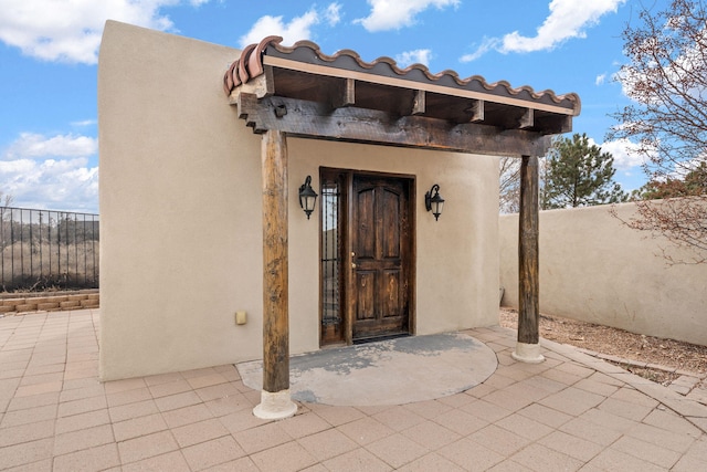 view of exterior entry featuring a patio area, fence, and stucco siding