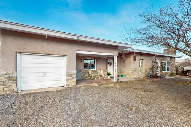 view of front of house featuring gravel driveway, stone siding, a garage, and stucco siding