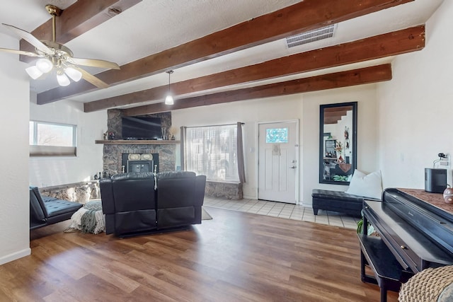 living area featuring baseboards, visible vents, wood finished floors, a fireplace, and beam ceiling