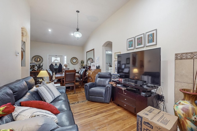 living room featuring light wood finished floors, arched walkways, and high vaulted ceiling