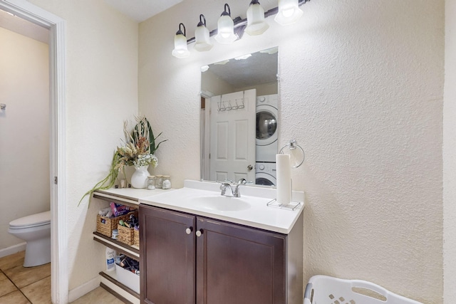 bathroom with baseboards, toilet, tile patterned flooring, vanity, and stacked washing maching and dryer