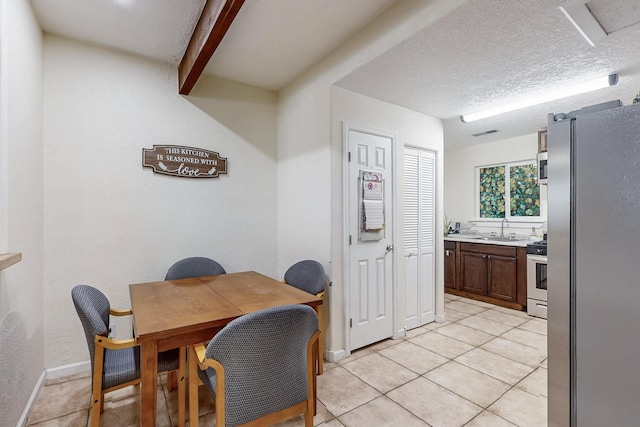 dining room featuring light tile patterned floors, a textured ceiling, visible vents, baseboards, and beamed ceiling