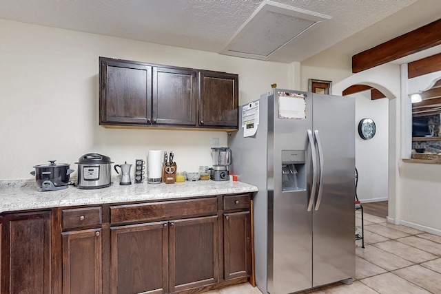 kitchen with light tile patterned floors, stainless steel fridge with ice dispenser, light countertops, dark brown cabinetry, and baseboards