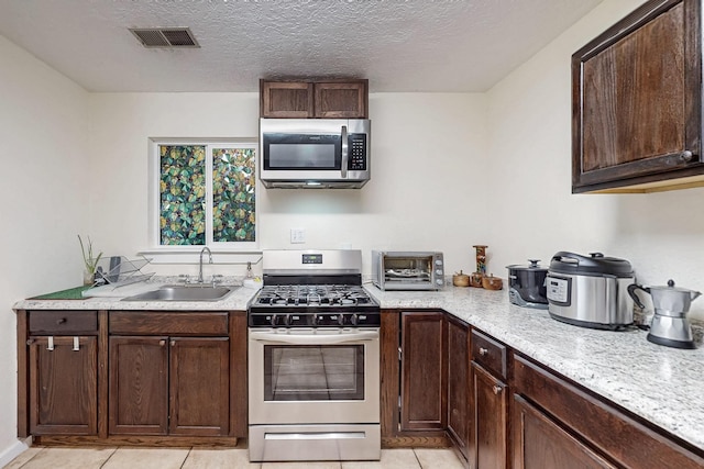 kitchen featuring visible vents, stainless steel appliances, dark brown cabinets, a textured ceiling, and a sink