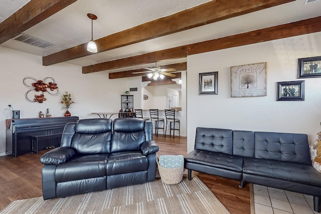 living area featuring beam ceiling, wood finished floors, and visible vents