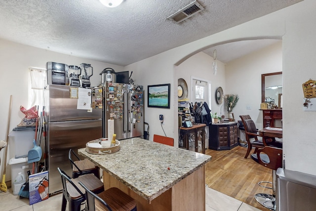 kitchen with arched walkways, visible vents, light wood-style floors, freestanding refrigerator, and light stone countertops