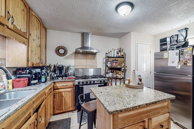 kitchen featuring a center island, stainless steel appliances, light tile patterned flooring, a sink, and wall chimney range hood