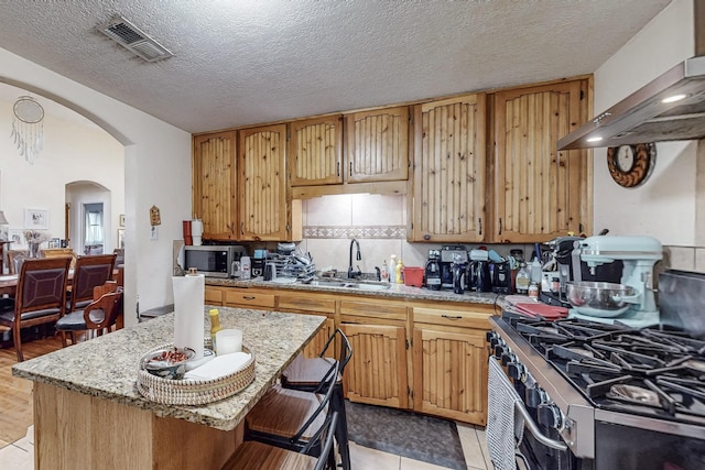 kitchen featuring arched walkways, visible vents, appliances with stainless steel finishes, a sink, and exhaust hood