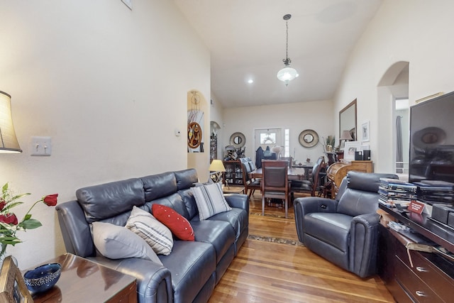 living area with arched walkways, high vaulted ceiling, and light wood-type flooring