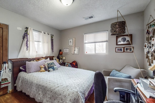 bedroom with dark wood-style floors, visible vents, and a textured ceiling