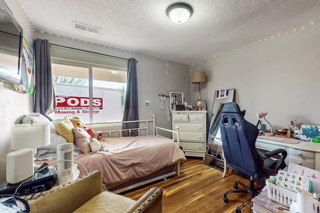 bedroom with visible vents, a textured ceiling, and wood finished floors