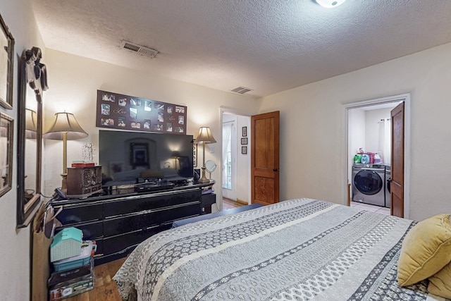 bedroom featuring a textured ceiling, visible vents, wood finished floors, and washing machine and clothes dryer