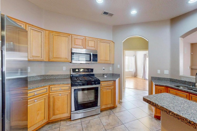 kitchen with dark countertops, arched walkways, stainless steel appliances, and a sink