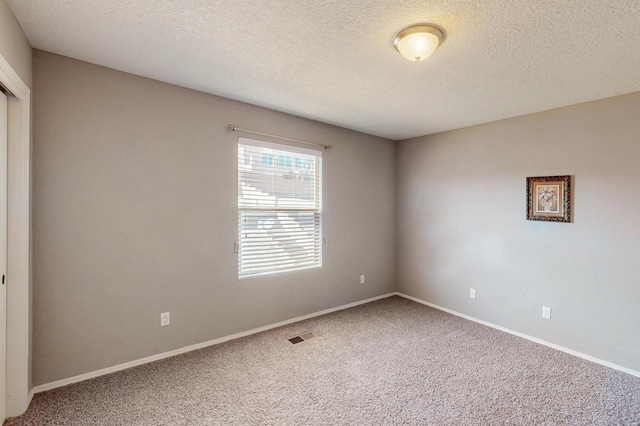 spare room with carpet floors, baseboards, visible vents, and a textured ceiling