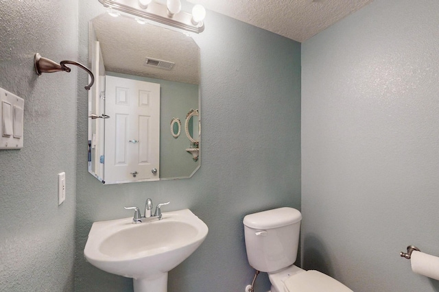 half bath featuring visible vents, a textured wall, toilet, a textured ceiling, and a sink