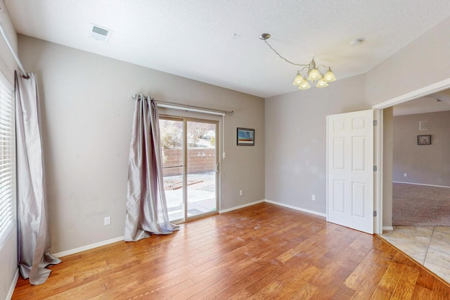 empty room featuring visible vents, a notable chandelier, baseboards, and wood finished floors