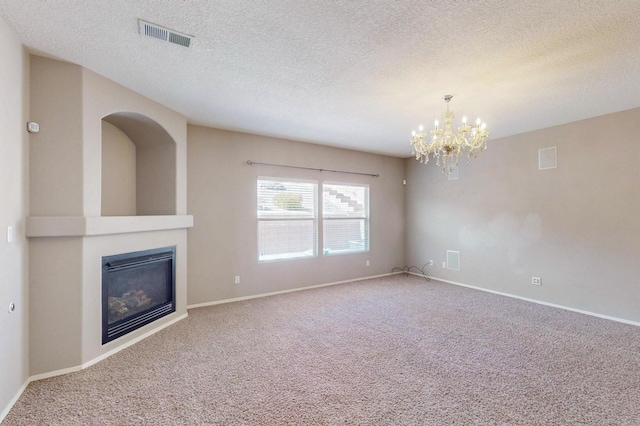 unfurnished living room with carpet floors, visible vents, a glass covered fireplace, a chandelier, and baseboards