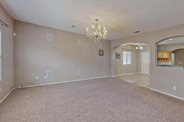 spare room with arched walkways, light colored carpet, and an inviting chandelier