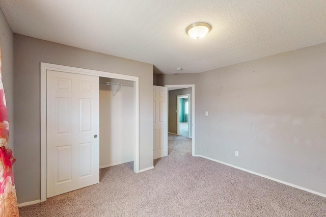 unfurnished bedroom featuring light carpet, a closet, a textured ceiling, and baseboards