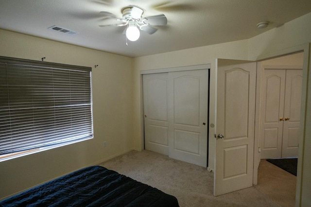 unfurnished bedroom featuring a ceiling fan, light colored carpet, a closet, and visible vents