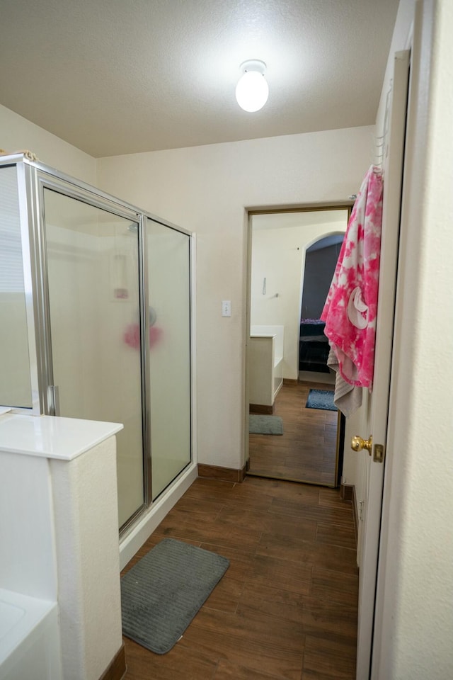 bathroom featuring ensuite bath, a shower stall, baseboards, and wood finished floors