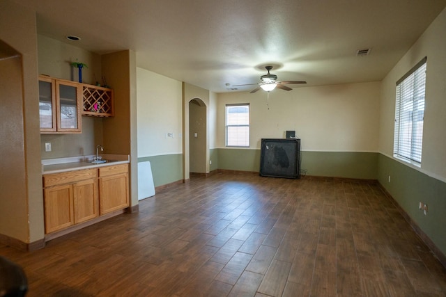 unfurnished living room featuring arched walkways, dark wood-type flooring, a sink, and a ceiling fan