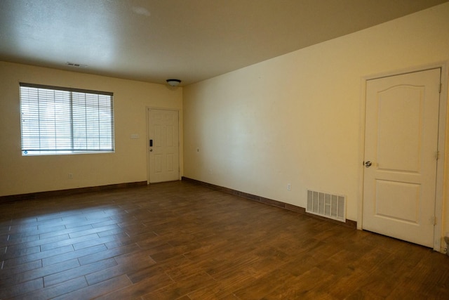 unfurnished room featuring dark wood-type flooring, visible vents, and baseboards