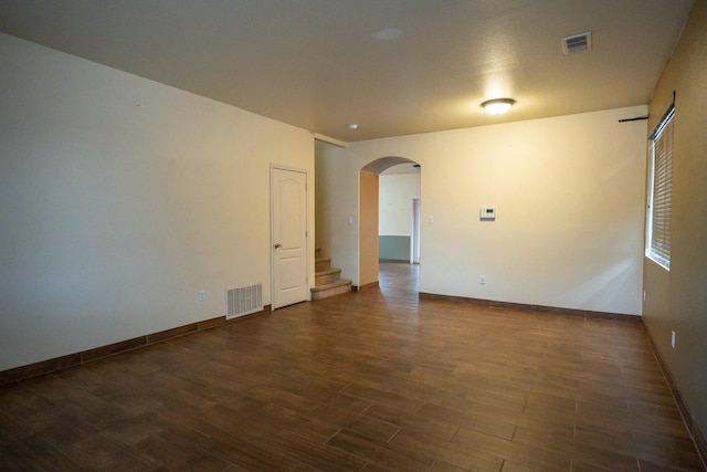 unfurnished room featuring arched walkways, dark wood finished floors, visible vents, and baseboards