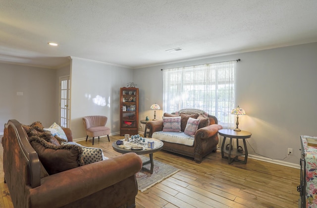 living area with visible vents, light wood-style flooring, ornamental molding, a textured ceiling, and baseboards