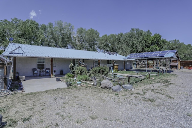 rear view of house featuring metal roof, solar panels, a patio area, and stucco siding