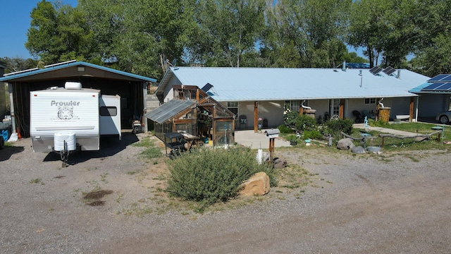 view of front of house with dirt driveway, a greenhouse, an outdoor structure, and a detached carport