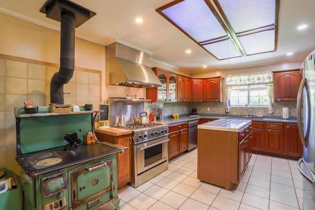 kitchen with stainless steel appliances, light tile patterned flooring, a sink, a kitchen island, and wall chimney exhaust hood