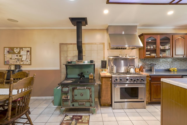 kitchen featuring range hood, tile countertops, high end stainless steel range, glass insert cabinets, and a wood stove