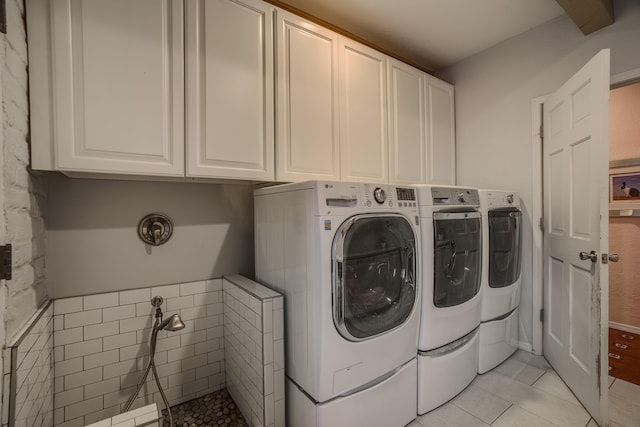 clothes washing area featuring washing machine and dryer, light tile patterned floors, and cabinets