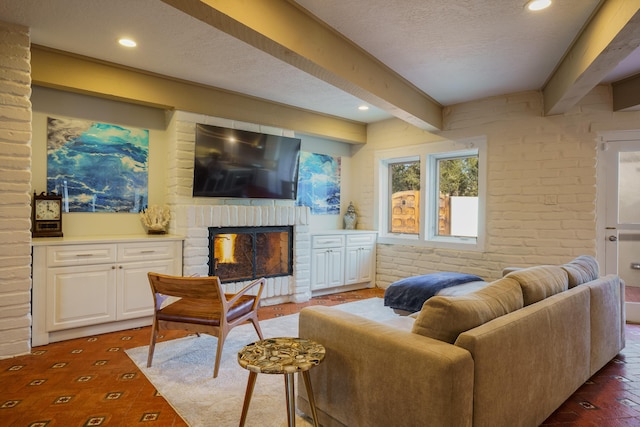 living room featuring a fireplace, beamed ceiling, brick wall, and a textured ceiling