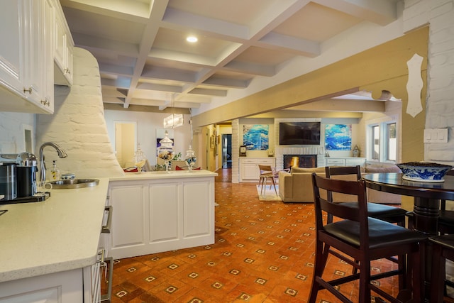 kitchen featuring a brick fireplace, sink, kitchen peninsula, white cabinets, and beam ceiling