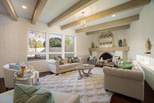 living room with a brick fireplace, an inviting chandelier, brick wall, wood-type flooring, and beamed ceiling