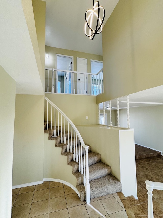 staircase with tile patterned flooring, a towering ceiling, and a chandelier